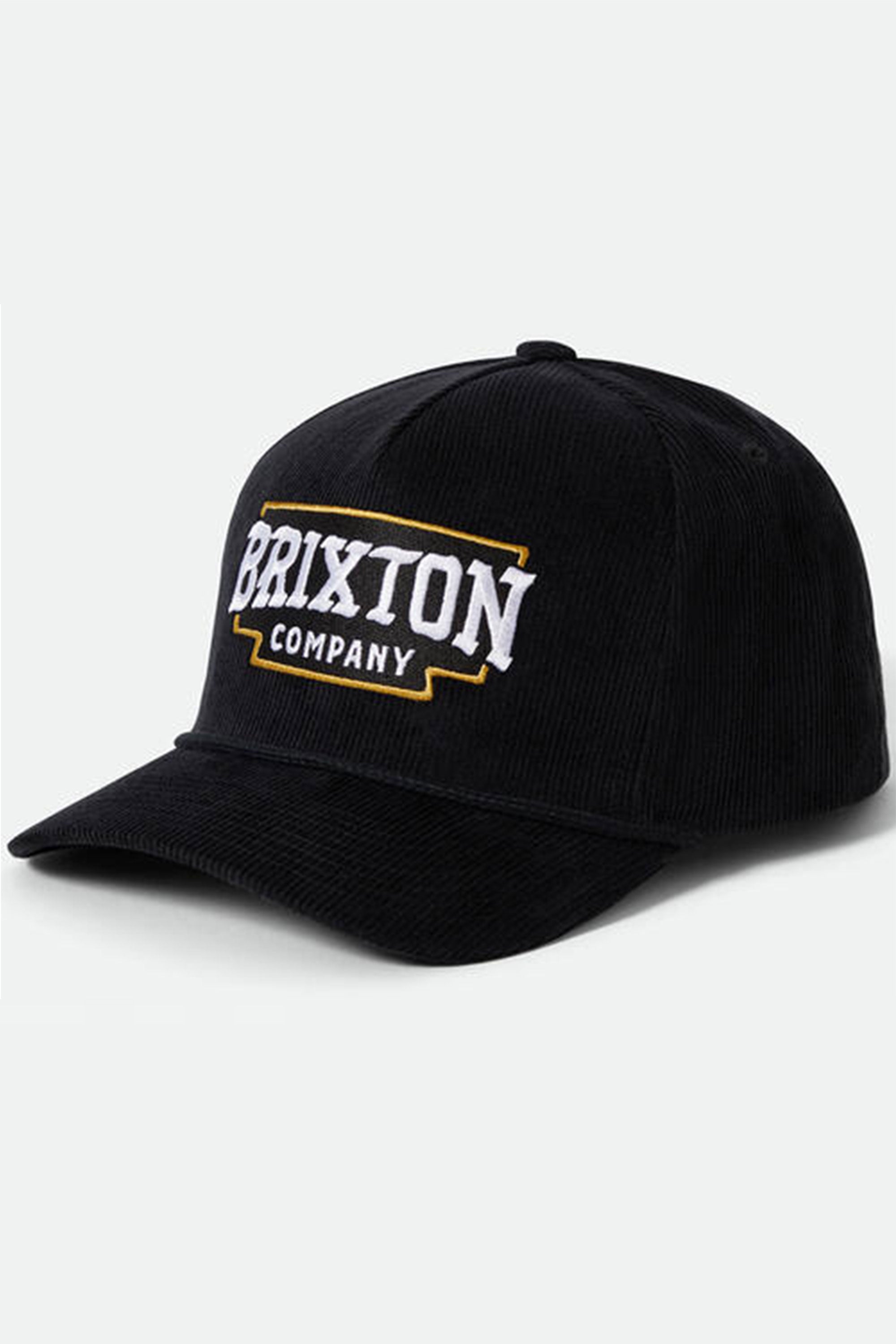 The Brixton Pierson Snapback is a black cotton corduroy hat with a curved brim, featuring bold white "BRIXTON" and smaller "COMPANY" text framed in yellow on the front. An adjustable snapback offers a comfortable fit.