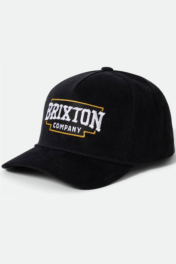 The Brixton Pierson Snapback is a black cotton corduroy hat with a curved brim, featuring bold white "BRIXTON" and smaller "COMPANY" text framed in yellow on the front. An adjustable snapback offers a comfortable fit.