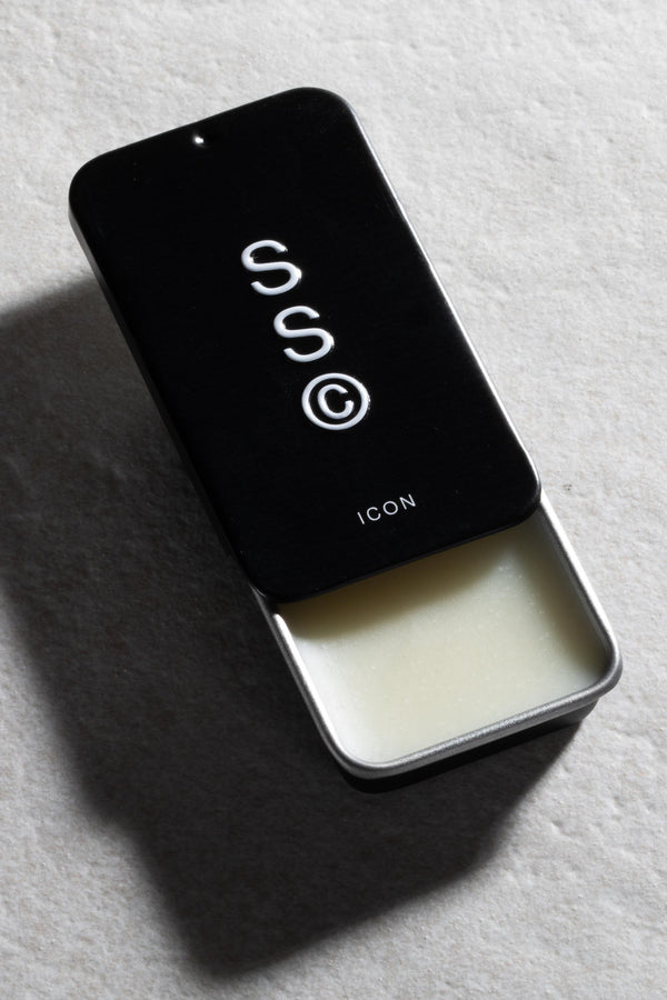 Solid State - Icon wax cologne in a black tin with white balm sits on a stone surface.