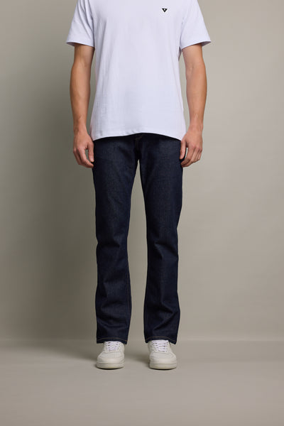 A person stands against a plain background wearing a white short-sleeve t-shirt, Barkers Wanderer Denim Straight Jean in dark blue, and white sneakers. The person's head is out of frame.