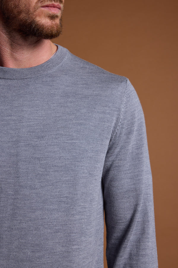 A man models the Barkers Skyland ZQrx Merino Crew, a light gray sweater made from ethically sourced merino wool. He stands against a plain brown background, with only his lower face, neck, and upper torso visible.