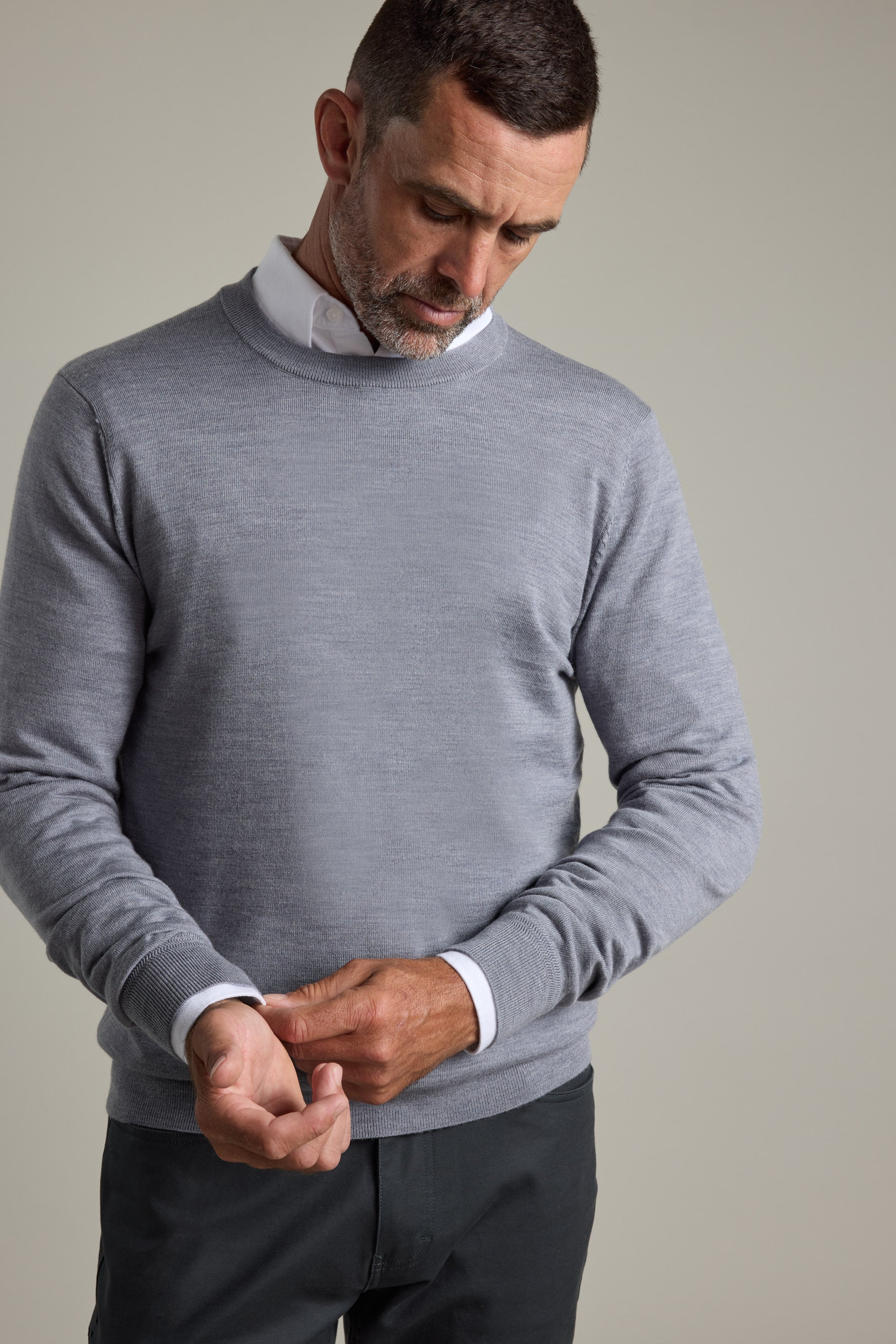 Man in a gray Barkers Skyland ZQrx Merino Crew sweater buttoning his cuff, looking down.