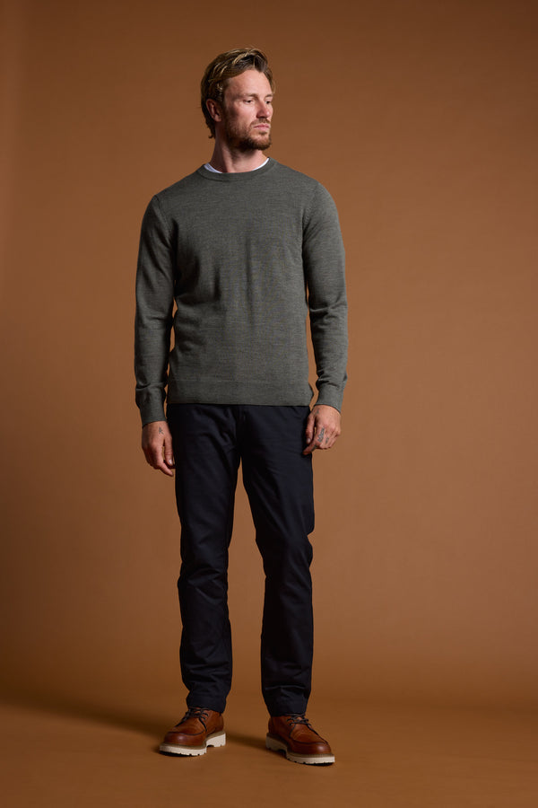A man with short hair and a beard stands against a plain brown background, wearing the Barkers Skyland ZQrx Merino Crew—a gray sweater made from ethically sourced merino—showcasing a modern, sustainable style.