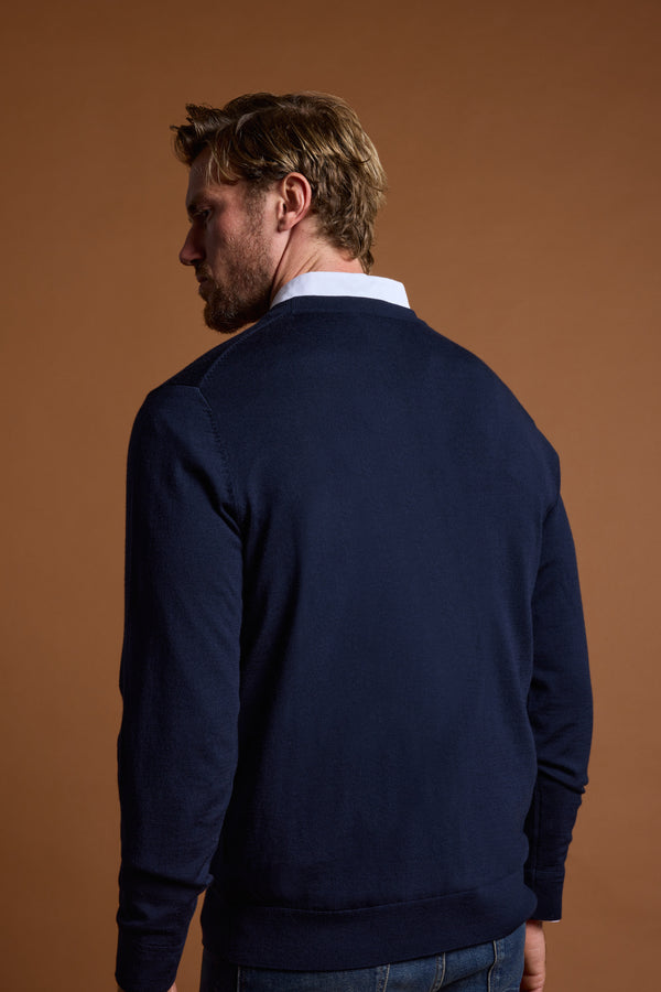 A man with light brown hair stands with his back to the camera, wearing the Barkers Skyland ZQrx Merino Crew sweater in navy over a white collared shirt, set against a plain brown background.