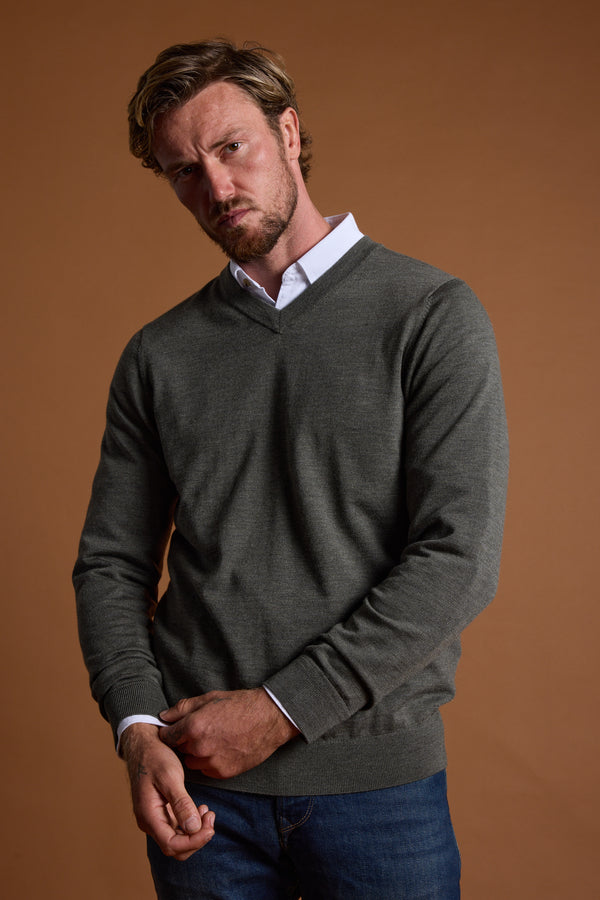 A light brown-haired, bearded man wears the Barkers Skyland ZQrx Merino Vee gray sweater over a white collared shirt and blue jeans, standing against a plain brown background with a slightly serious expression.