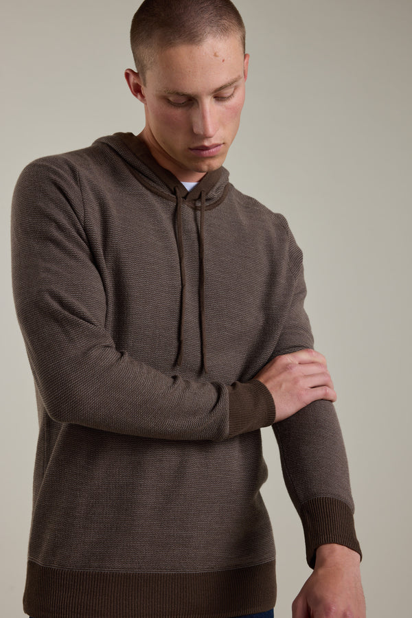 A person in a Barkers Roxbury Merino Hoody with ribbed cuffs and hem looks down, touching their left forearm, set against a plain light background.