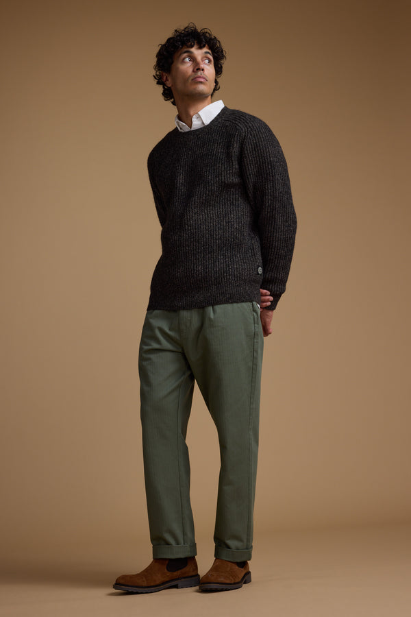 Person in dark sweater, Barkers Wadley Twill Pant, and brown shoes stands against brown background.