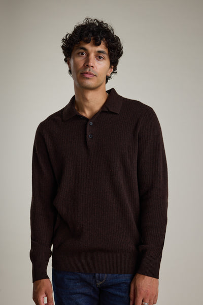 A man with curly dark hair wears the Barkers Braxton Merino Long Sleeve Polo, featuring ribbed detailing and buttons, standing against a plain light background.