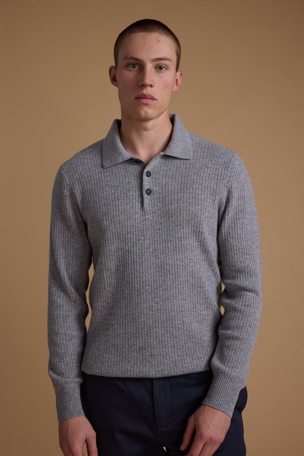 A young man with short hair stands against a beige background, wearing the Barkers Braxton Merino Long Sleeve Polo in light gray and dark pants, looking directly at the camera with a neutral expression.