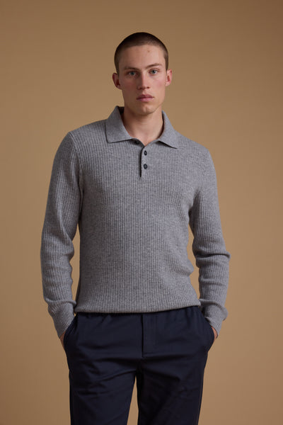 A young man with short hair wears the Barkers Braxton Merino Long Sleeve Polo in light gray and dark navy pants, standing with hands in pockets against a plain beige background.