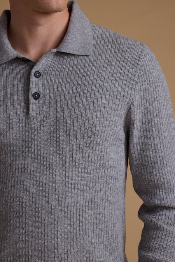A person wears the Barkers Braxton Merino Long Sleeve Polo in light gray, featuring a ribbed knit design, collar, two buttons, and ribbed detailing, shown from shoulders to waist against a beige background.