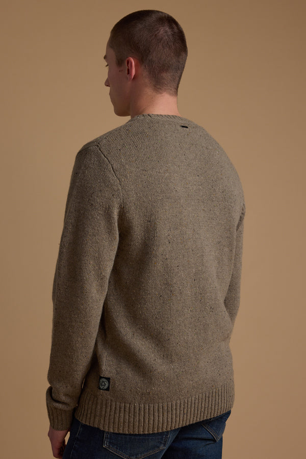 A person with short hair is seen from behind, wearing the Barkers Anglers Merino Crew sweater in brown and blue jeans, standing against a plain beige background.