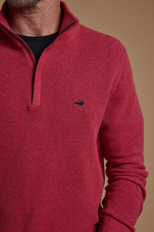 A person models the Barkers Ketch Cotton 1/4 Zip in dark pink over a black shirt, shown from shoulders to waist against a tan background, with only the lower face and neck partially visible.