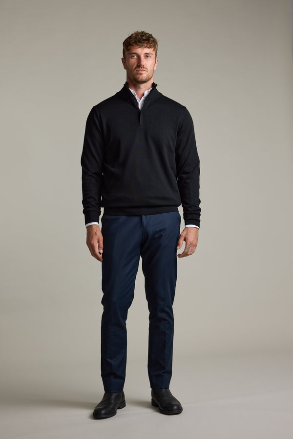A man wears a Barkers Skyland ZQRX Merino 1/4 Zip and blue pants against a plain background.