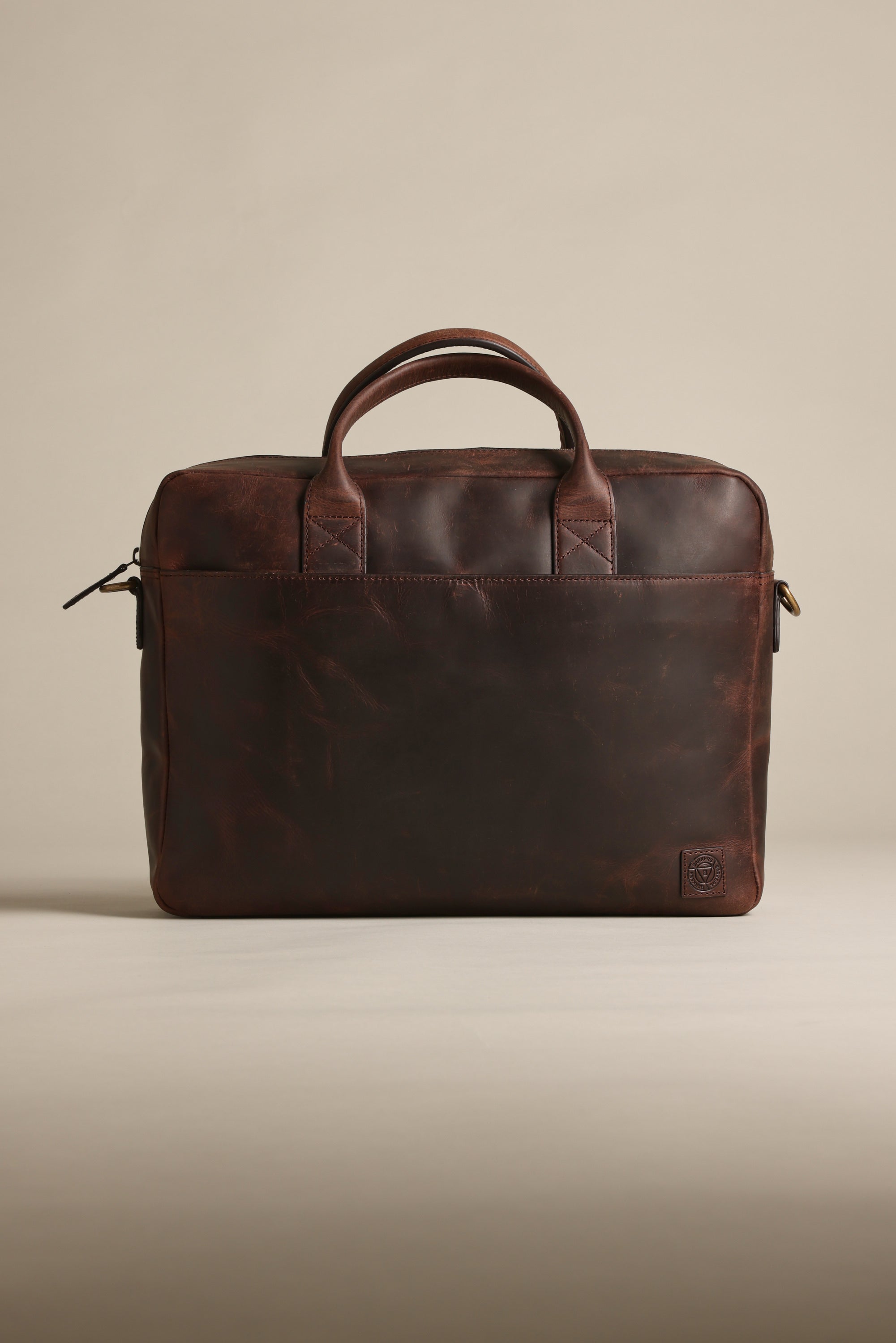 The Barkers Wilkinson Leather Laptop Bag, in dark brown quality leather, features two handles, a zippered top, and a subtle embossed logo in the lower corner, shown against a plain beige background.