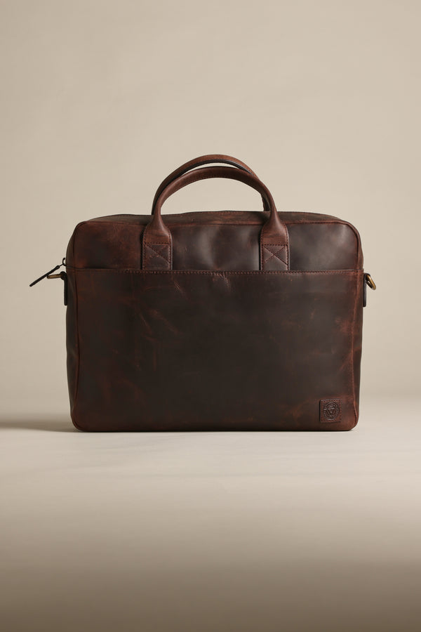 The Barkers Wilkinson Leather Laptop Bag, in dark brown quality leather, features two handles, a zippered top, and a subtle embossed logo in the lower corner, shown against a plain beige background.