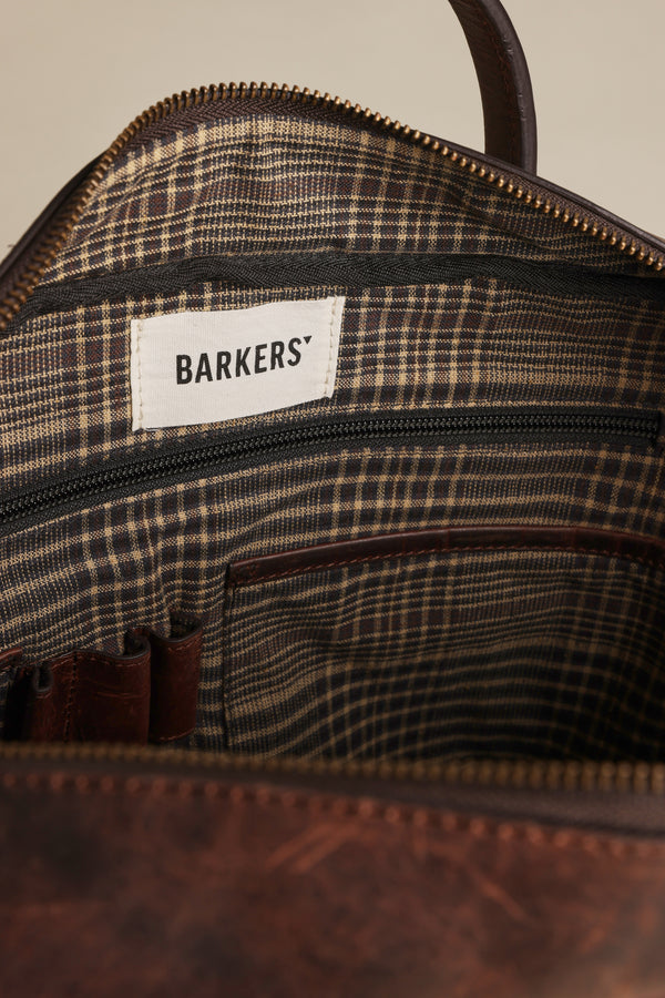 Close-up of the Wilkinson Leather Laptop Bag by Barkers, showing its plaid fabric lining, zippered pockets, and a white Barkers label.