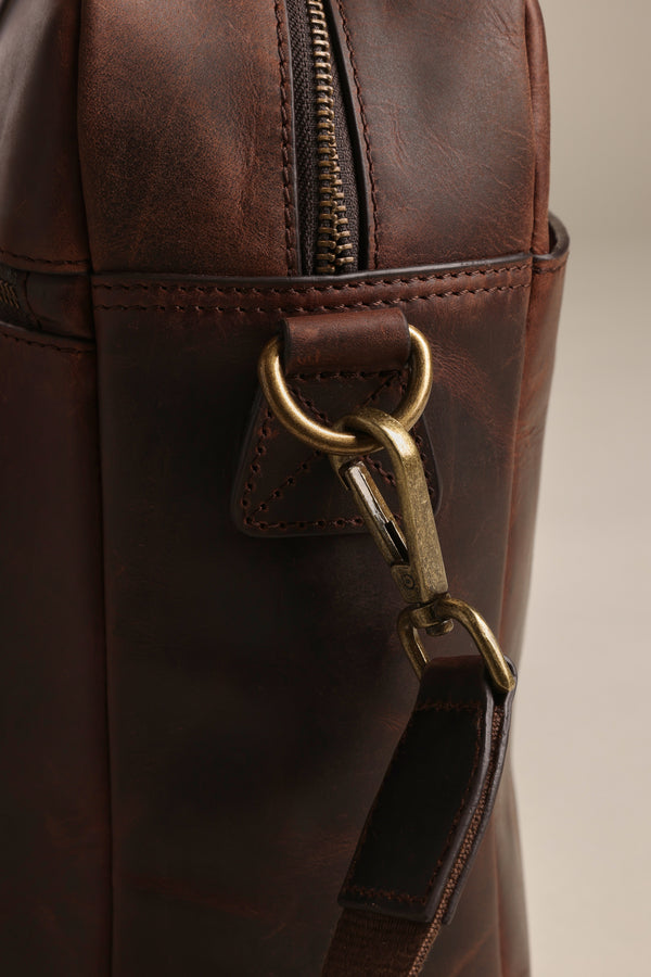 Close-up of the Barkers Wilkinson Leather Laptop Bag showcases a metal zipper and a brass swivel clasp on its matching leather strap.