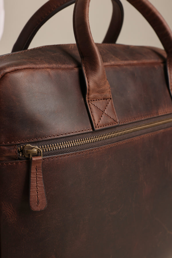 Close-up of the Barkers Wilkinson Leather Laptop Bag, highlighting its sturdy handle, metal zipper with leather pull tab, and textured leather surface.