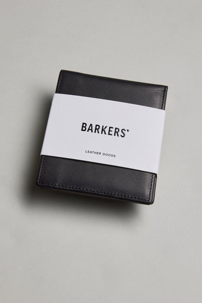 A black Harris Leather Fold Wallet by Barkers, wrapped in a white paper band with the brand name, is placed on a light gray surface.