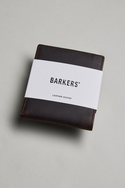 A dark brown Harris Leather Fold Wallet by Barkers, wrapped with a white paper band labeled BARKERS LEATHER GOODS, rests on a light gray surface.
