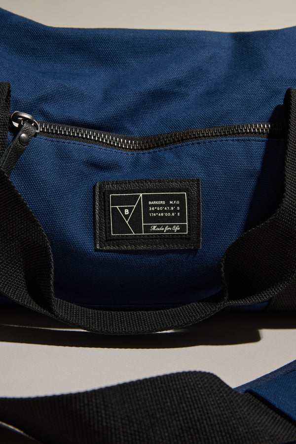 Close-up of Barkers Canvas Duffle Bag in blue with black zipper and Barkers label.
