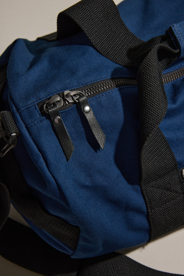 Barkers Canvas Duffle Bag in blue cotton with black straps and zippers on a neutral background.
