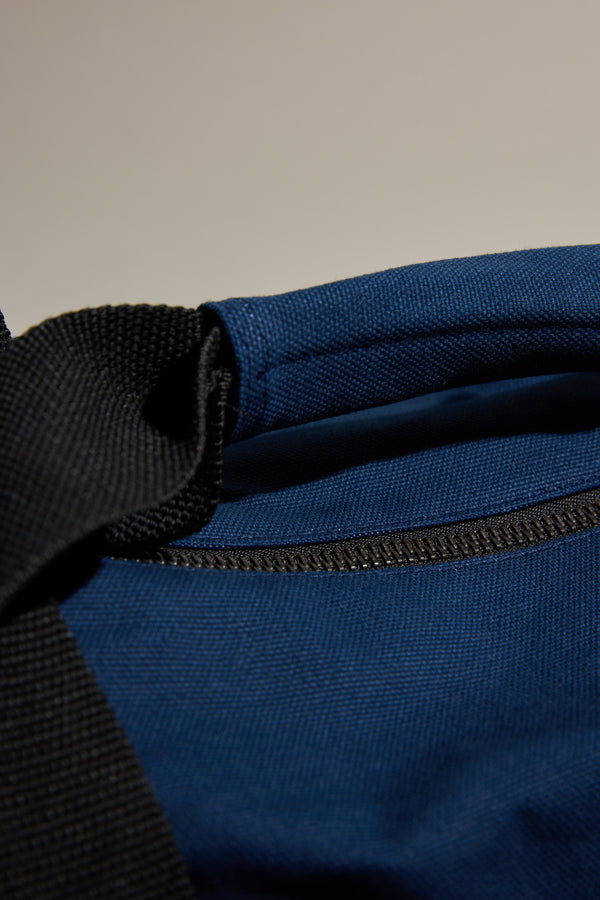 Close-up of Barkers Canvas Duffle Bag in blue with black strap on a plain background.