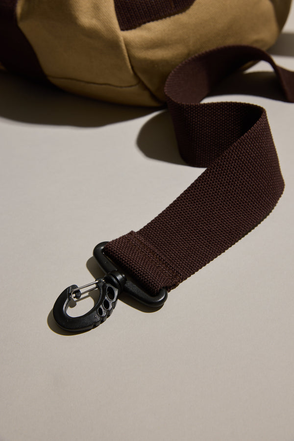 Close-up of Barkers Canvas Duffle Bag brown strap with black clip on a beige surface.