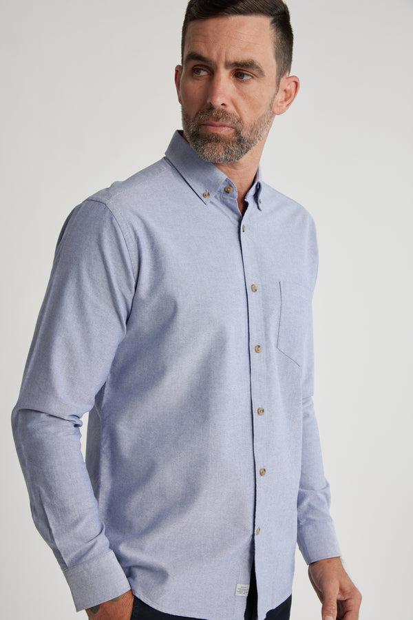 A man with short brown hair and a beard wears the Barkers Thatcher Oxford Shirt in a tailored fit, made from responsibly sourced cotton, as he stands against a plain light background looking slightly to the side.