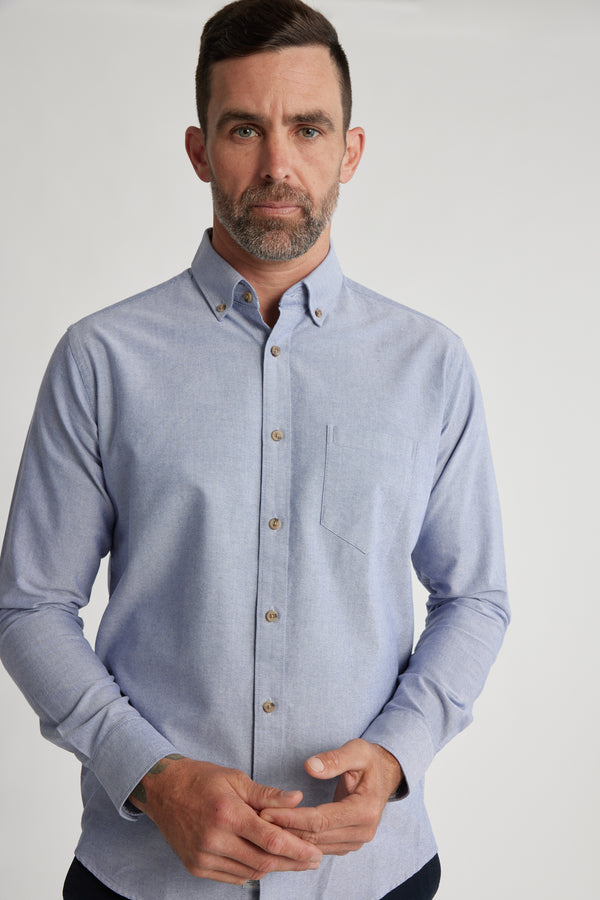 A man with short dark hair and a beard wears the Barkers Thatcher Oxford Shirt, a light blue tailored fit made from responsibly sourced cotton, standing against a white background and looking directly at the camera.