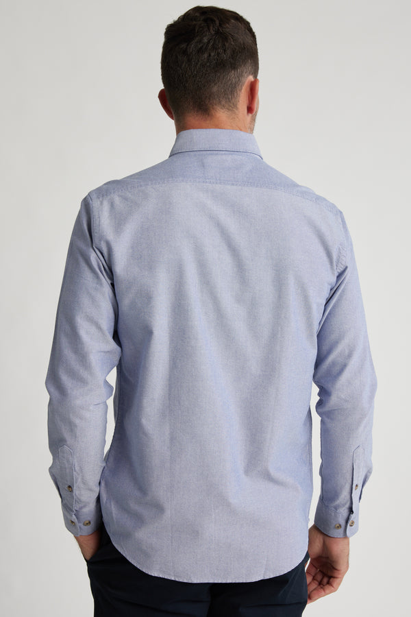 A man with short brown hair is seen from behind wearing the Barkers Thatcher Oxford Shirt in light blue and dark pants, standing against a plain light background.