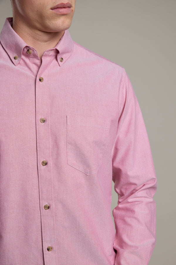 A person wearing the Barkers Thatcher Oxford Shirt in light pink, responsibly sourced cotton, with a chest pocket and tailored fit, is shown from shoulders to waist against a plain background. Their face is partially visible.