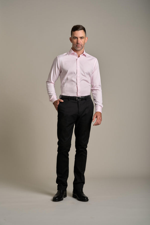 A man stands against a plain light background wearing a Barkers Tribeca Reg Cuff Shirt in light pink, black pants, and black shoes, with one hand in his pocket and a neutral expression.