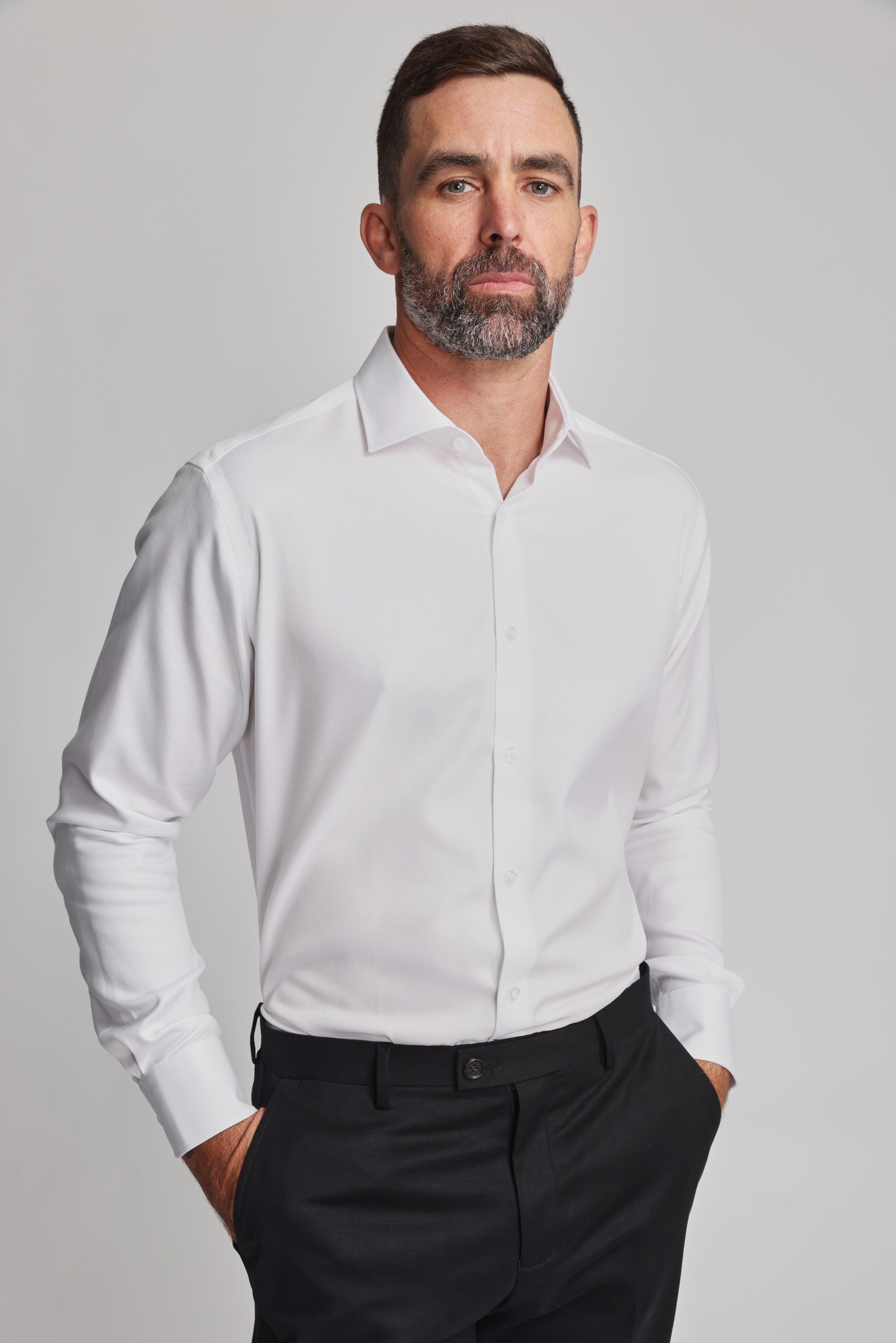 A man with short dark hair and a beard wears the Barkers Mexted Texture Shirt in white and black pants, standing with his hands in his pockets against a plain light background.