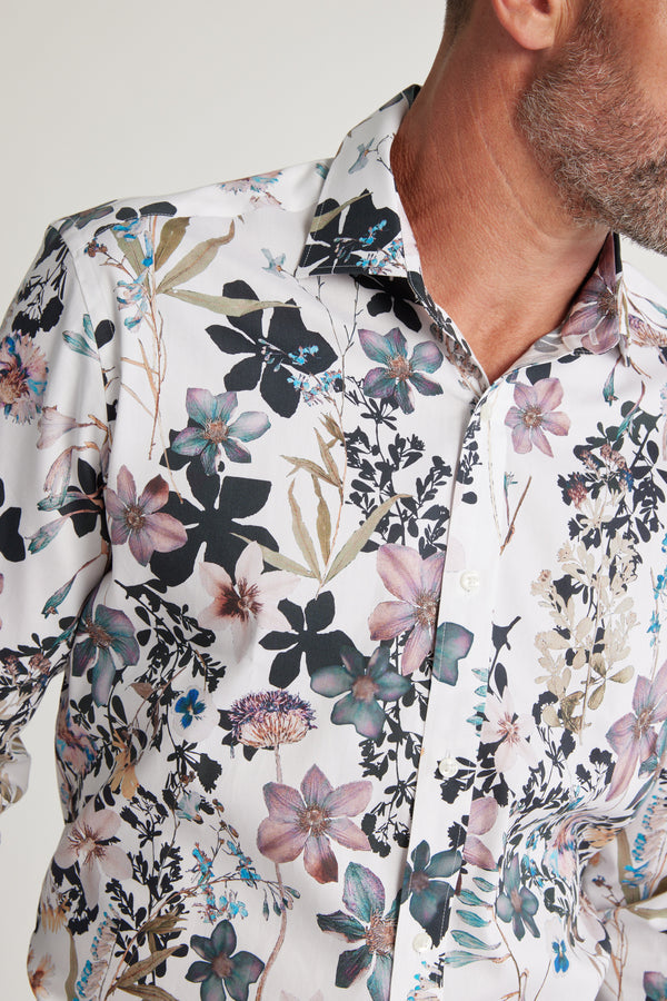 A man wears the Barkers Apothecary AOP Business Shirt, featuring a bold purple, blue, and black floral pattern. Made from responsibly sourced cotton, the shirt combines standout style with sustainability.