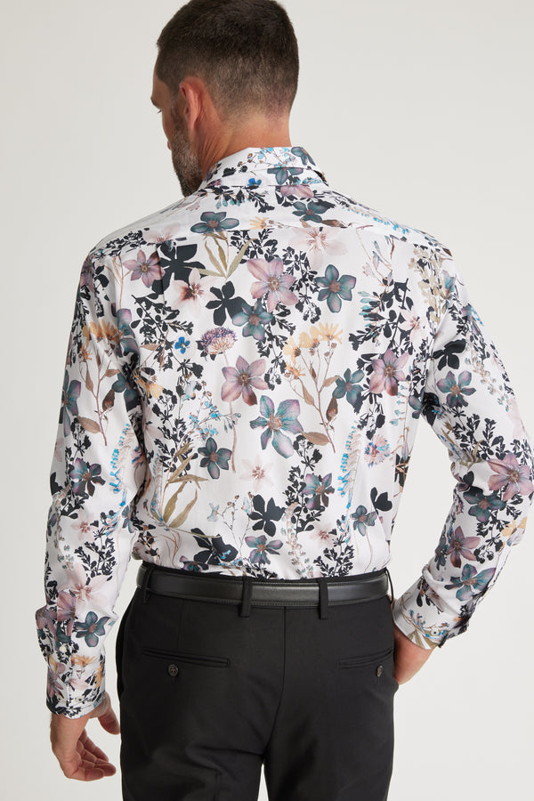 A man with short dark hair, seen from behind, wears a Barkers Apothecary AOP Business Shirt with a colorful floral print and black trousers against a plain white background.