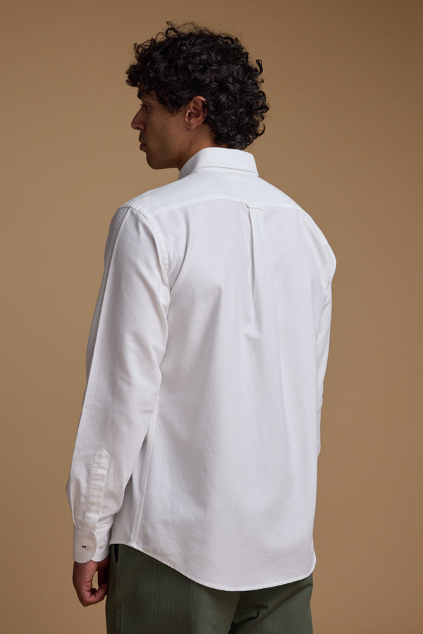 A person with short, curly dark hair is shown from the back, wearing a classic fit white Barkers Maynard Oxford Shirt made from responsibly sourced cotton and green pants against a plain beige background.