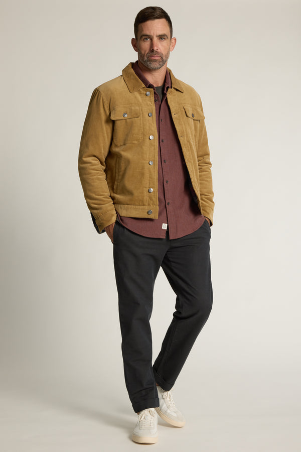 Man in a tan Barkers Raleigh Oxford Overshirt, maroon shirt, dark pants, and white sneakers stands.