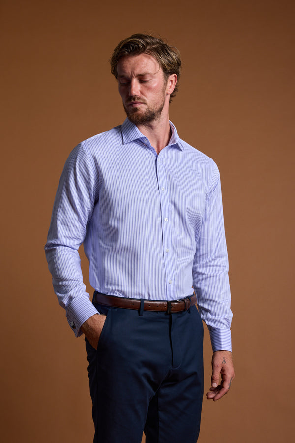 A man with light brown hair and a short beard wears the Barkers Asmara French Cuff Business Shirt with navy trousers, standing with one hand in his pocket against a plain brown background.
