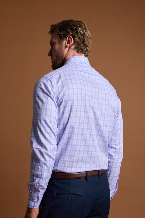 A man is seen from behind wearing the Barkers Larry Check Business Shirt, featuring a light blue and pink plaid pattern, tucked into navy pants with a brown belt, standing against a plain brown background.