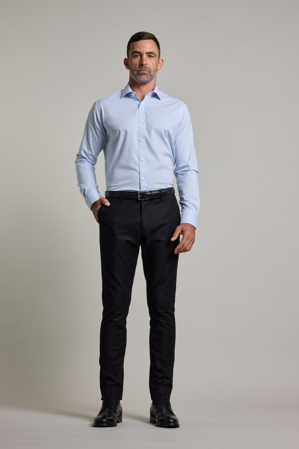 A man stands facing forward against a plain background, wearing the Barkers Hunter Check Business Shirt with black pants, a belt, and black dress shoes. One hand is in his pocket and he has a neutral expression.