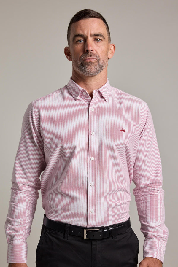 A man with short hair and a trimmed beard wears the Barkers Maynard Oxford Stripe Shirt, a light pink, classic fit men's cotton shirt with thin stripes, tucked into black pants and paired with a black belt against a neutral background.