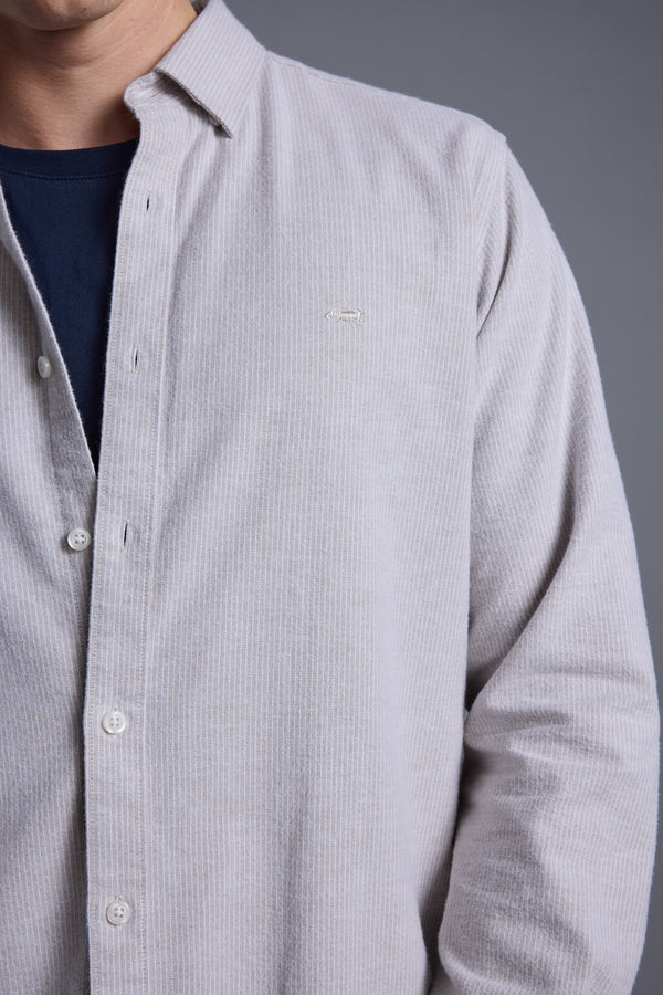 Wearing the Barkers Maynard Oxford Stripe Shirt—light gray with vertical stripes, made from responsibly sourced cotton—over a dark blue T-shirt. Shown from shoulders to waist against a plain gray background; face partially out of frame.