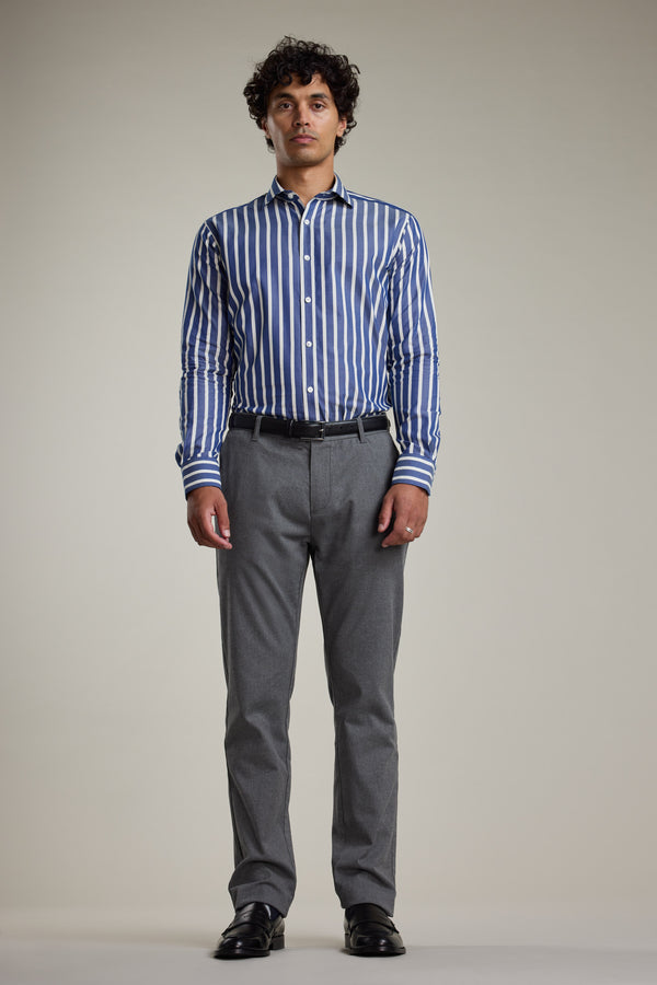 A man faces forward against a plain light background, wearing Barkers' Nandas Stripe Business Shirt in blue and white, which is wrinkle resistant, paired with gray trousers and black dress shoes.