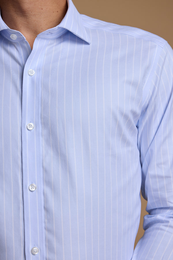 Close-up of a person wearing the Barkers Goodall Stripe Business Shirt, a light blue, long-sleeve wrinkle-free shirt with thin white stripes and white buttons, shown against a beige background with only the torso and neck visible.