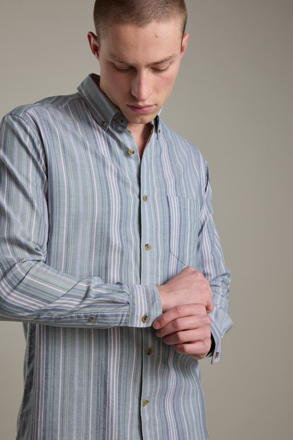 Wearing the Barkers Huntley Striped Oxford Shirt in light blue and gray, a person with a tailored fit looks down as they adjust their cuff against a plain background.