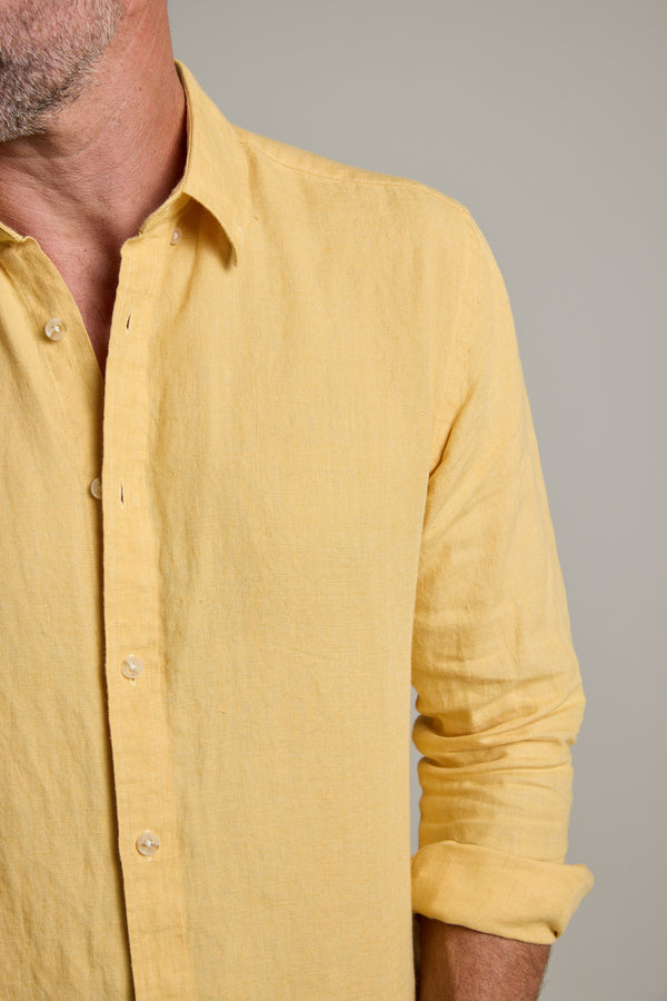 A person wears a light yellow, long-sleeve Dorset Linen Shirt by Barkers with sleeves rolled up, shown from shoulders to waist. The tailored fit gives a crisp look; the face is partially out of frame.