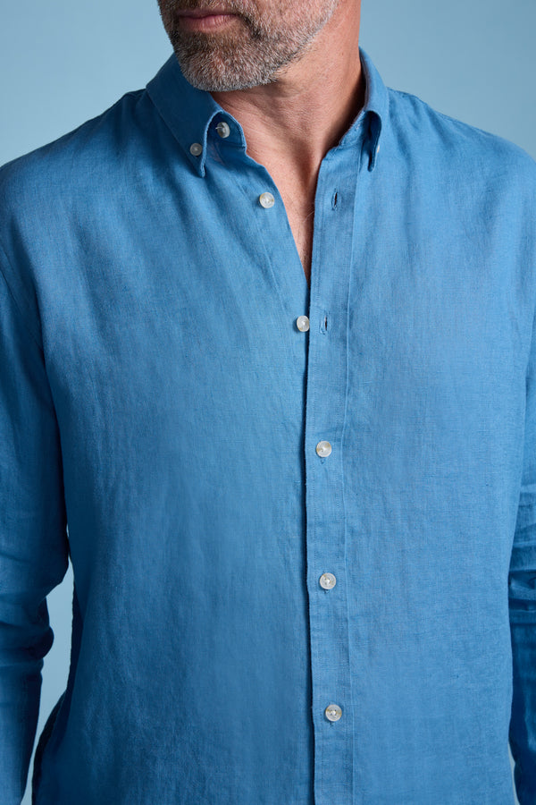 A man with a short beard wears the Barkers Dorset Linen Shirt in blue with a tailored fit, standing against a light blue background; his face is partially out of frame.