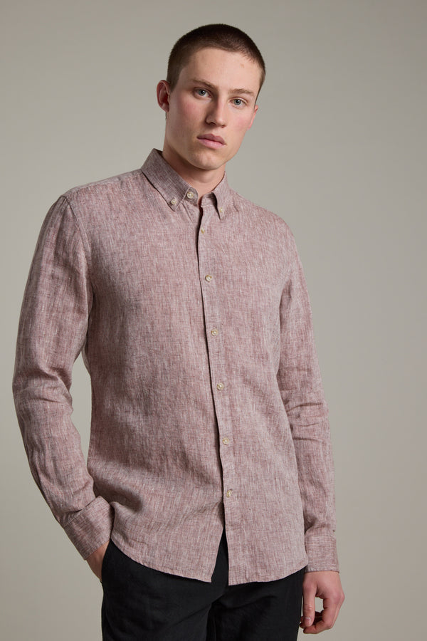 A young man with short hair wears the Barkers Dorset Linen Shirt, a tailored-fit light red long-sleeve option, paired with black pants, standing against a plain light gray background with one hand in his pocket.